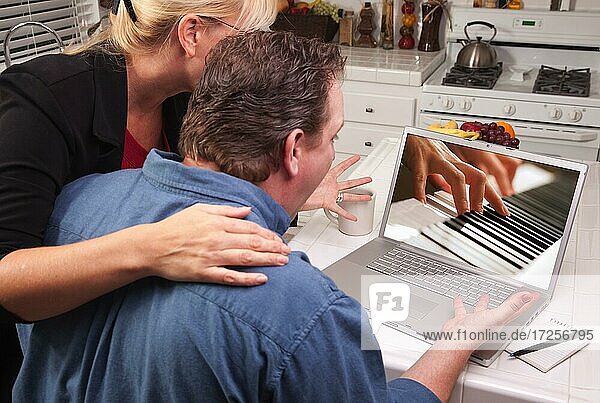 Couple in kitchen using laptop with piano performer on the screen