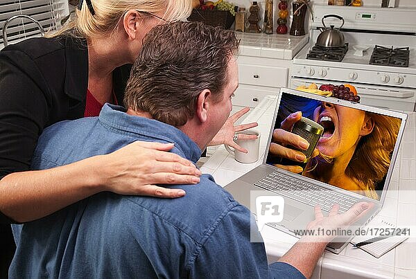 Couple in kitchen using laptop with singing woman on the screen