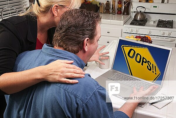 Couple in kitchen using laptop with yellow oops road sign on the screen