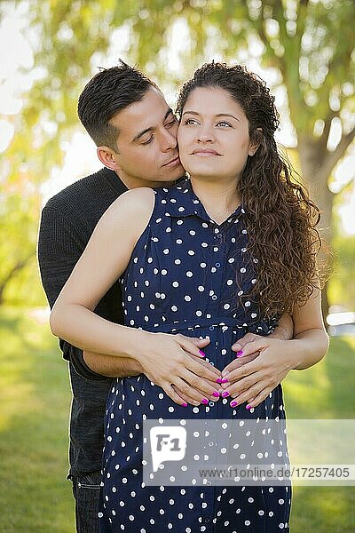 Glücklicher hispanischer Mann umarmt seine schwangere Frau im Freien im Park