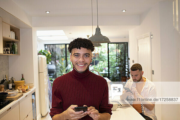 Porträt glücklich zuversichtlich junger Mann mit Smartphone in der Küche