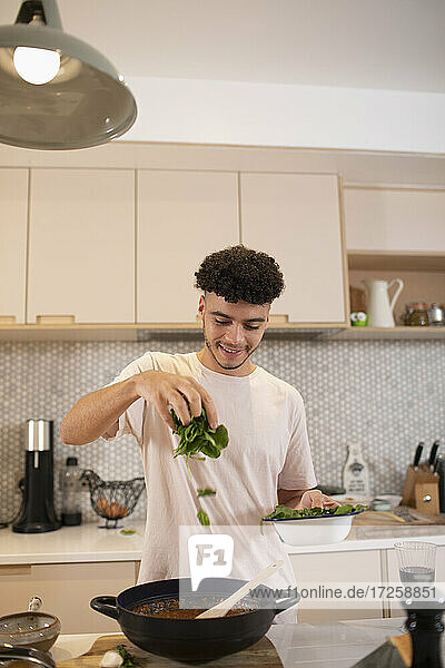Lächelnder junger Mann kocht mit frischem Basilikum in der Küche