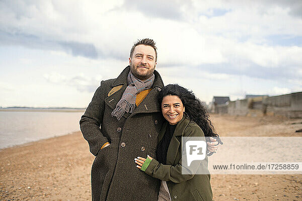 Portrait happy affectionate couple in winter coats hugging on beach
