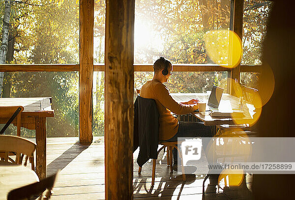Geschäftsmann mit Kopfhörer arbeiten am Laptop in sonnigen Cafe