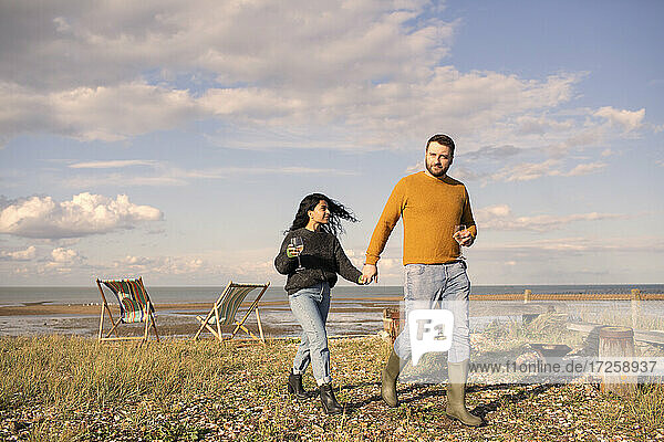 Glückliches Paar mit Wein halten Hände zu Fuß auf sonnigen Strand