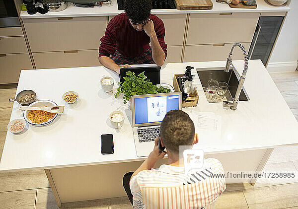 Junges schwules männliches Paar arbeitet von zu Hause aus an Laptops in der Küche