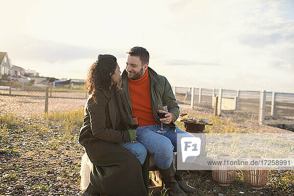 Happy romantic couple enjoying wine by fire on winter beach patio