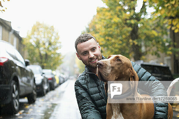 Glücklicher junger Mann mit Hund auf nassen städtischen Straße