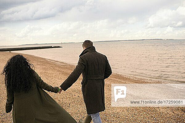 Zärtliches Paar  das sich an den Händen hält  geht am Strand des Wintermeeres spazieren