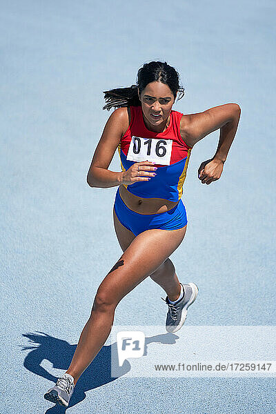 Determined female track and field athlete running on sunny track