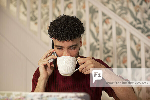 Junger Mann mit Kaffee im Gespräch auf Smartphone arbeiten am Laptop