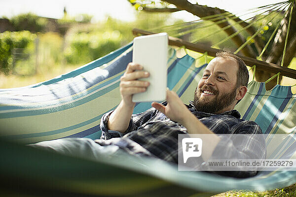 Happy man using digital tablet in sunny summer hammock