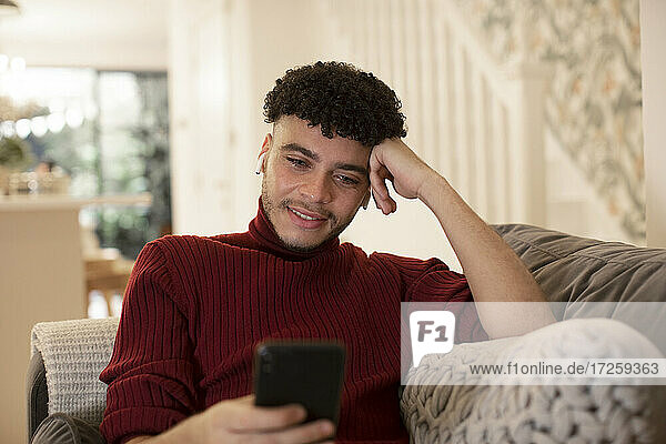 Young man using smart phone on living room sofa