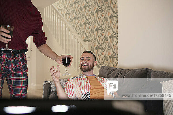 Happy gay male couple enjoying red wine and watching TV at home