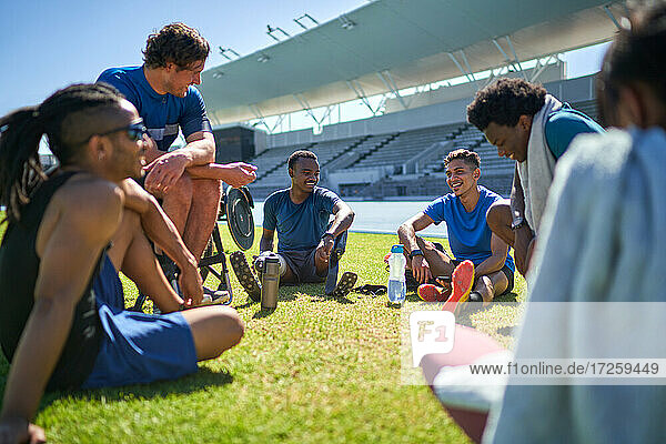 Junge männliche Sportler Freunde ausruhen und reden auf sonnigen Stadion Rasen