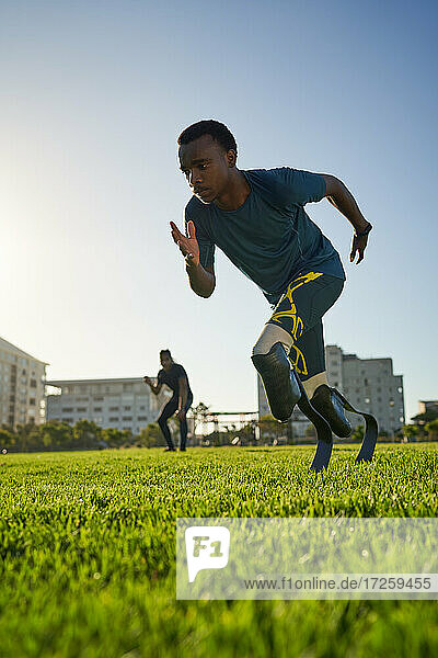 Focused male amputee sprinter training in sunny sports field