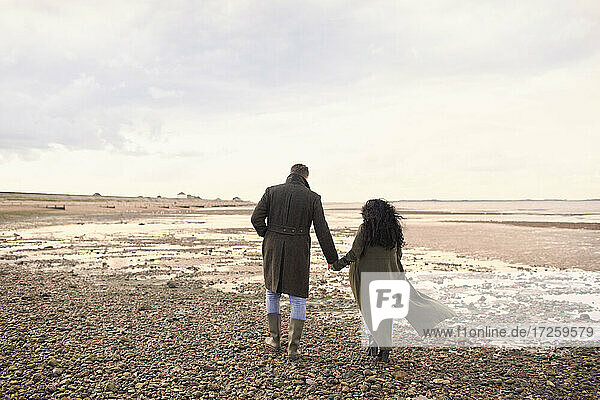 Couple in winter coats holding hands walking on ocean beach