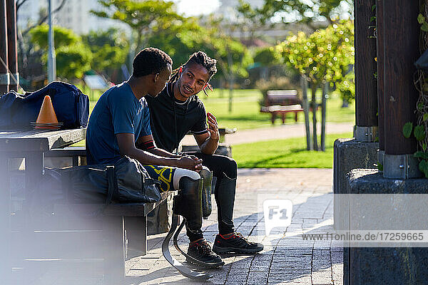 Coach and young male amputee athlete talking on park bench