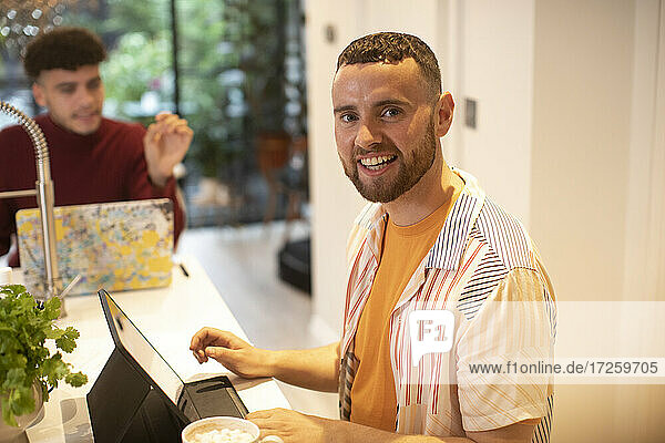 Porträt glücklicher junger Mann  der in der Küche an einem digitalen Tablet arbeitet
