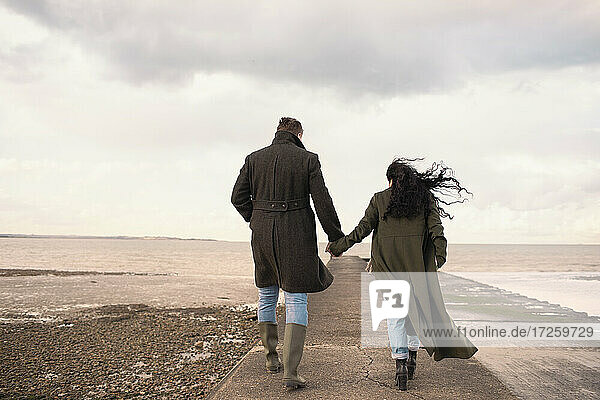 Paar in Wintermäntel halten Hände auf Ozean Strand Steg