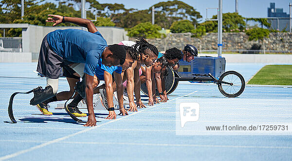 Vielfältige Athleten stehen an der Startlinie auf der sonnigen blauen Sportbahn bereit