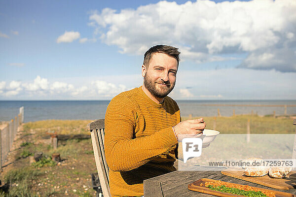 Porträt glücklich Mann Essen auf sonnigen Ozean Strand Terrasse