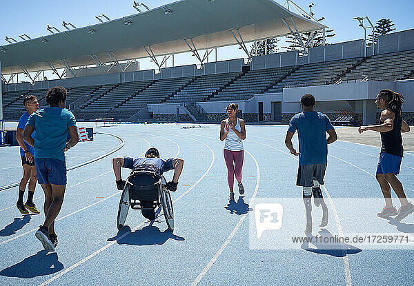 Junge  vielseitige Athleten wärmen sich auf der sonnigen blauen Stadion-Sportbahn auf