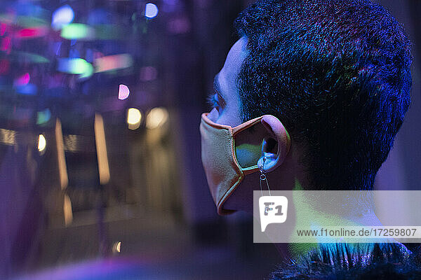 Junger Mann mit Sicherheitsnadel-Ohrring trägt Gesichtsmaske in Nachtclub