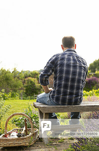 Mann macht eine Pause von der Gartenarbeit auf der Bank im sonnigen Sommergarten