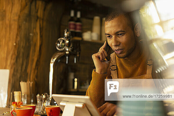 Männlicher Café-Besitzer  der eine Bestellung per Telefon am digitalen Tablet entgegennimmt