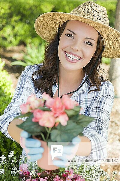 Attraktive glückliche junge erwachsene Frau mit Hut und Handschuhen bei der Gartenarbeit im Freien
