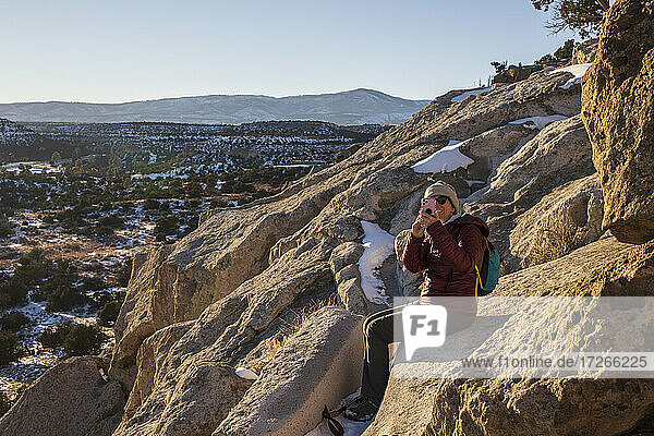 USA  New Mexico  Los Alamos  Bandelier national Monument  Tsankwai  Frau sitzt auf Felsen und fotografiert mit Smartphone