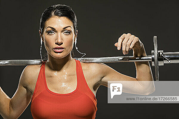 Studio portrait of athletic woman in red sleeveless top with barbell