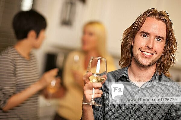 Lächelnder junger Mann mit einem Glas Wein  der in einer Party-Einstellung gesellig ist
