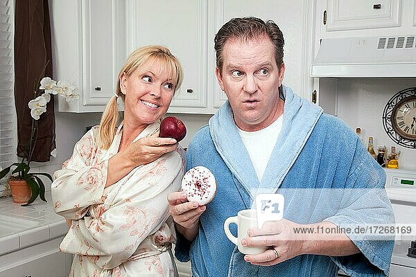 Couple in kitchen eating donut and coffee or healthy fruit