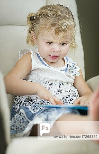 Adorable blonde haired blue eyed little girl reading her book in the chair