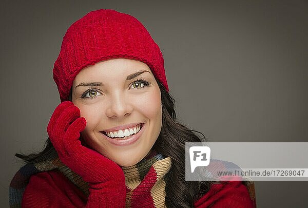 Glückliche gemischtrassige Frau mit Wintermütze und Handschuhen auf grauem Hintergrund
