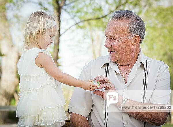 Nettes Baby Mädchen Handing Osterei zu Großvater draußen im Park