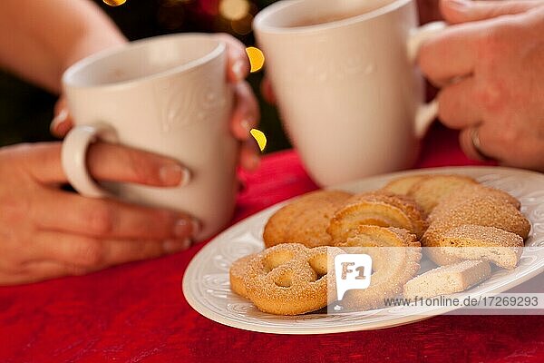 Mann und Frau teilen heiße Schokolade und Kekse vor der Weihnachtsbeleuchtung