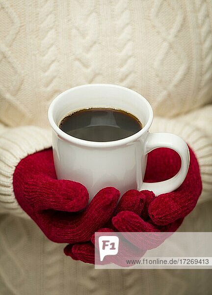 Frau im Pullover mit saisonalen roten Fäustlingen hält eine warme Tasse Kaffee
