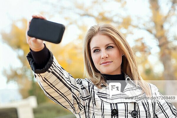 Pretty young woman taking picture with camera phone in the park one fall day