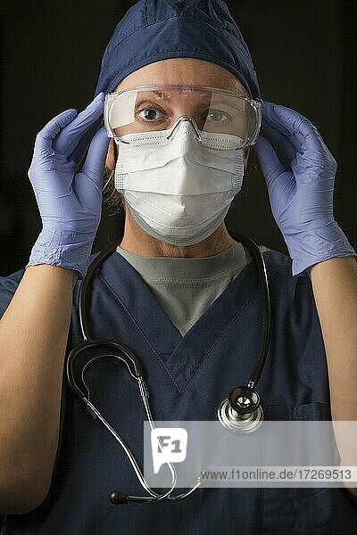 Besorgte Ärztin oder Krankenschwester  die eine Gesichtsschutzkleidung anlegt