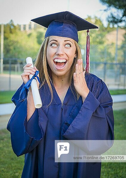 Excited and expressive young woman holding diploma in cap and gown outdoors