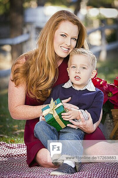 Handsome young boy holding christmas gift with his mom in the park