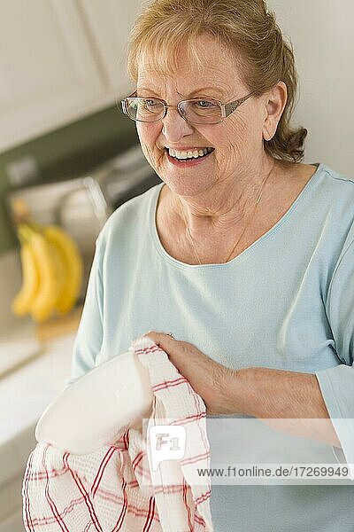 Lächelnde ältere Frau trocknet Schüssel an Spüle in Küche