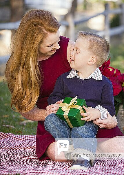Handsome jungen Jungen hält Weihnachtsgeschenk mit seiner Mutter im Park