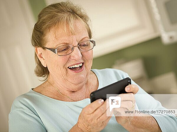 Glückliche ältere Frau  die auf ihrem intelligenten Mobiltelefon in der Küche SMS schreibt