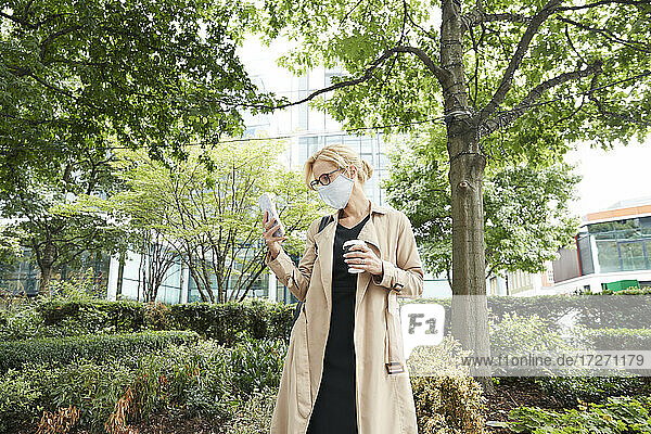 Geschäftsfrau hält Kaffeetasse  während sie ein Mobiltelefon in der Stadt benutzt