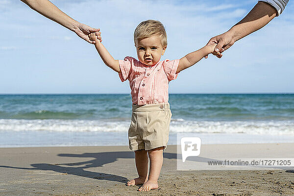Eltern halten die Hände eines kleinen Jungen am Strand