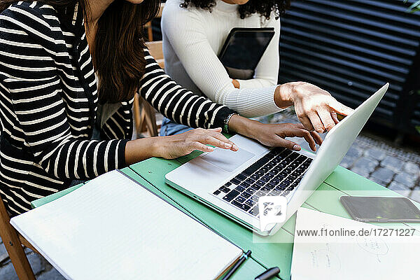 Weibliche Kollegen benutzen einen Laptop  während sie auf einem Tisch in einem Café sitzen